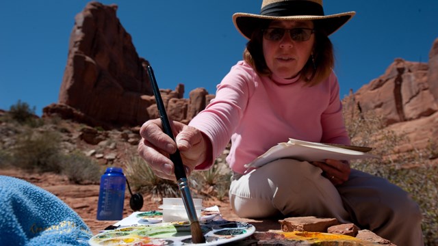 A woman dips a brush into a palette of paints
