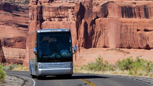 a bus driving on a road with red rock walls in the background