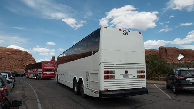 a white tour bus with a tall stone arch in the background