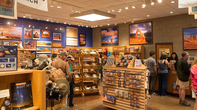 people walk around shelves in a bookstore. banners hang overhead with posters on the wall