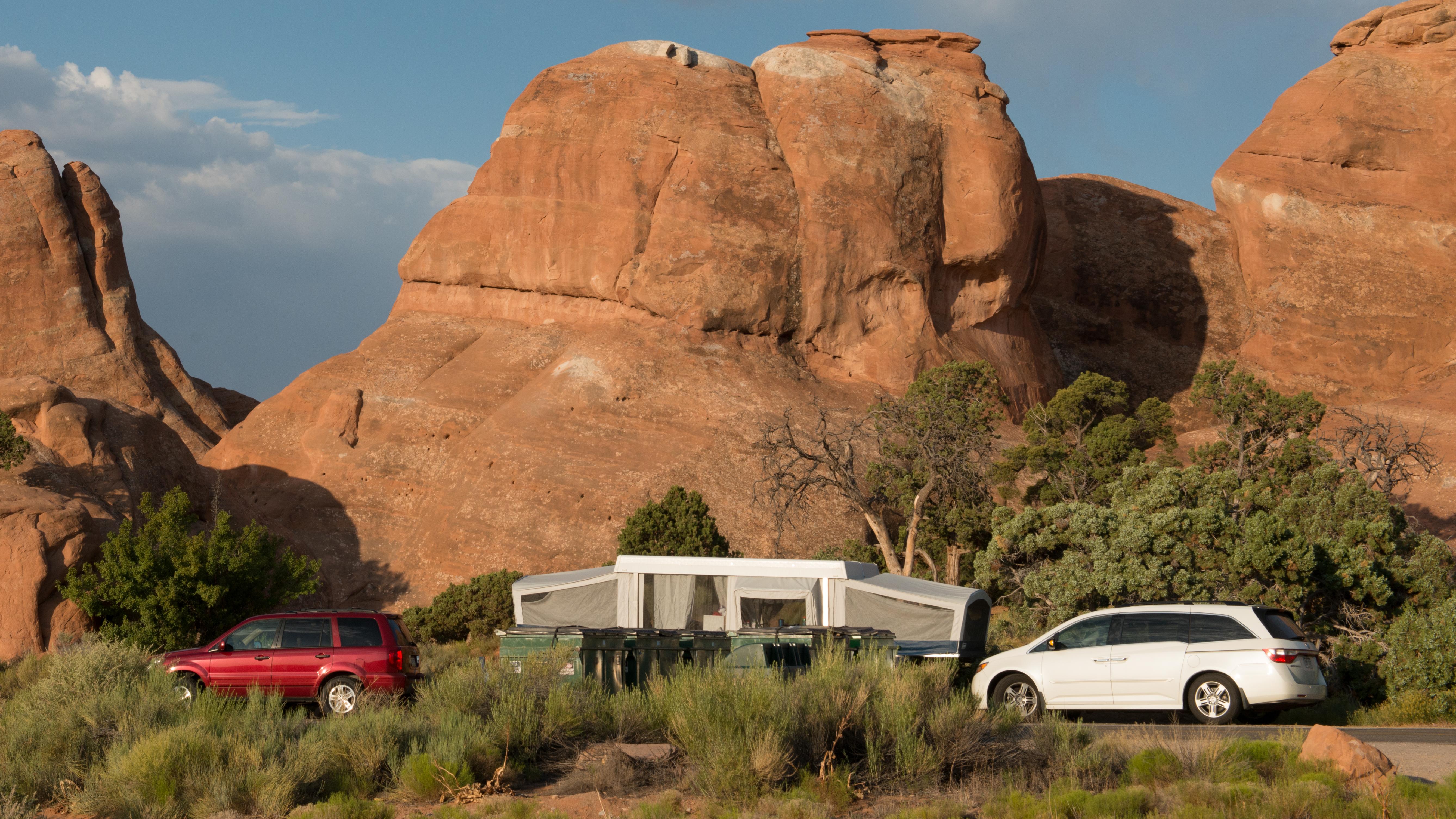 a pop-up trailer and two vehicles in front of red rock cliffs
