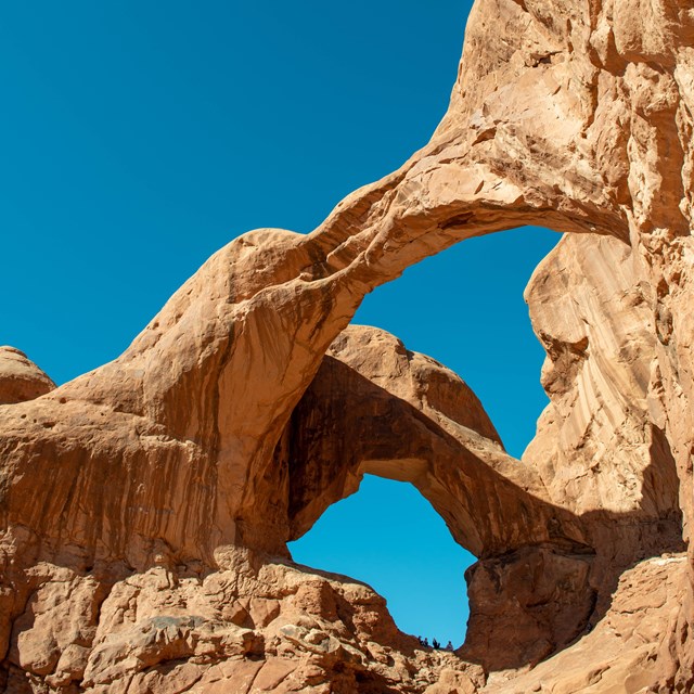 Brown sandstone arches span a bright blue sky