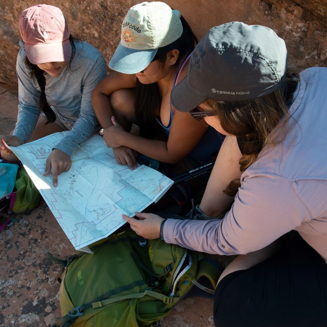 Three hikers look at a map to see where they're headed next
