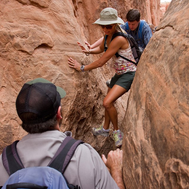 two people scramble through a narrow gap in the rocks