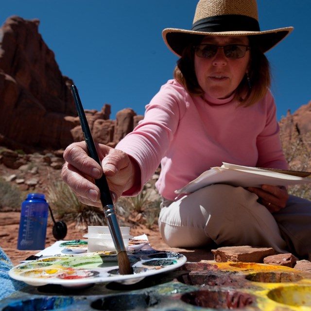 A woman dips a brush into a palette of paints
