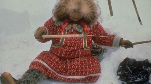 A woman ice fishing in traditional Arctic clothing.