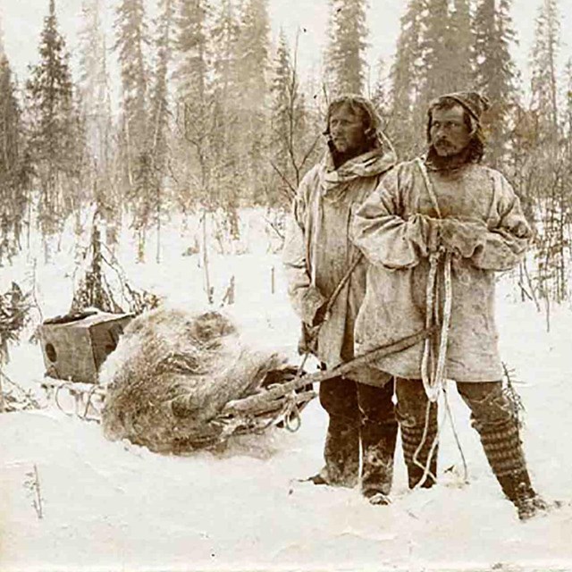 Historic image of people traveling by sled across snow-covered landscape.