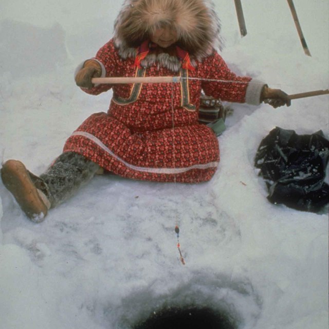 A woman ice fishing in traditional Arctic clothing.