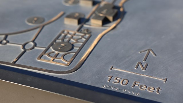 A bronze relief map with buildings, roads, and a legend with braille labels.