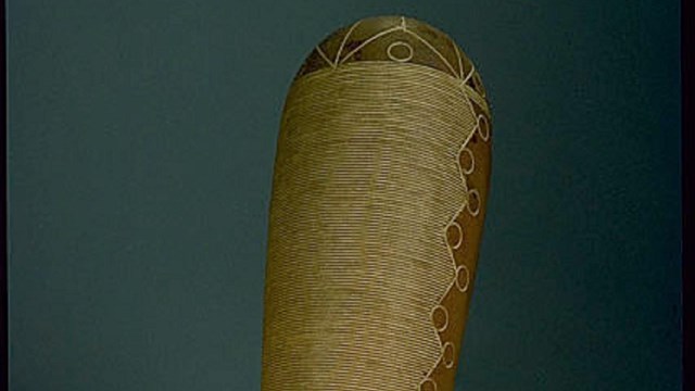 A guiro stands upright on a gray surface. It is a curved gourd shape with carved ridges along it.