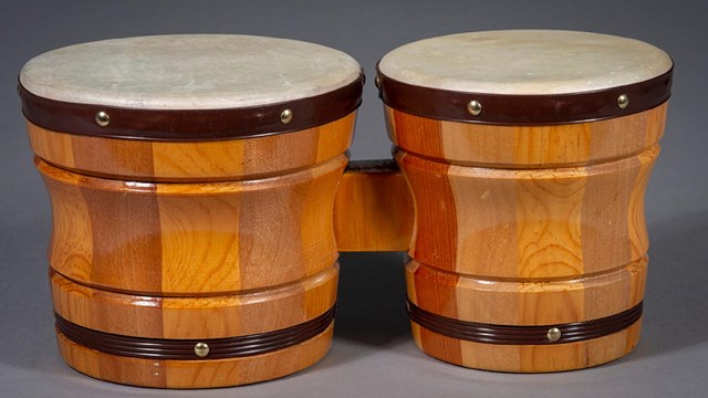 A set of bongo drums connected with a piece of wood rests on a gray surface.