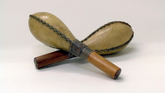 Two maracas are propped up against one another on a white surface.