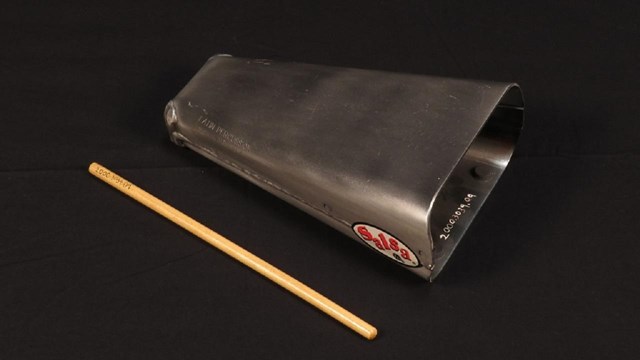 A black cowbell rests on a black surface. 