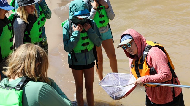 A scientists holds a net up to a group of students.