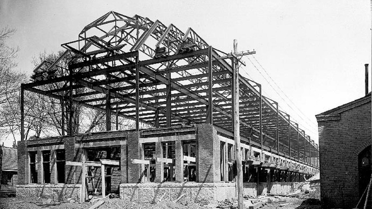 A black and white photograph of a steel frame of a large rectangular building.