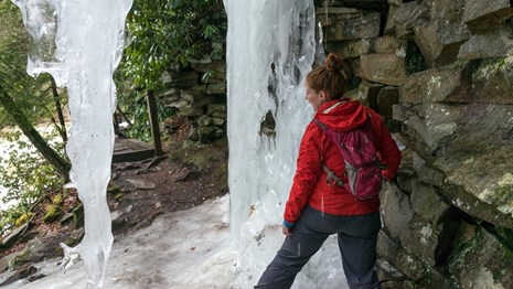 Hiker standing next to ice hanging from a rock outcrop over a trail