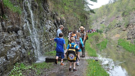 Ranger talking to an adult and group of kids on a trail between a rock face and canal