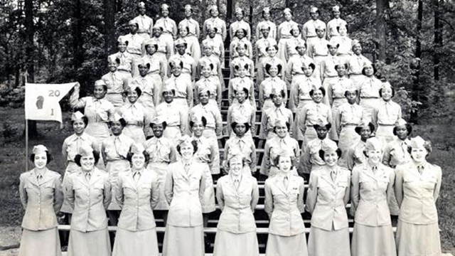 Women in light colored military uniforms standing in rows on bleachers