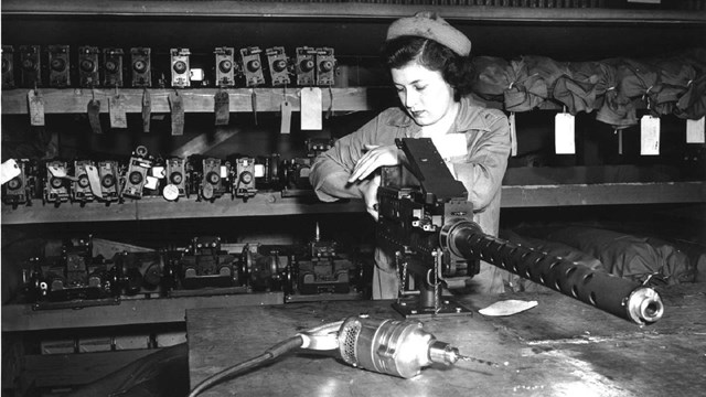 White woman adjusting machine gun with shelves of machinery behind her