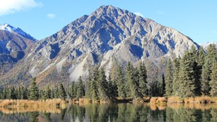 Image of calm lake with trees and mountains in the background.