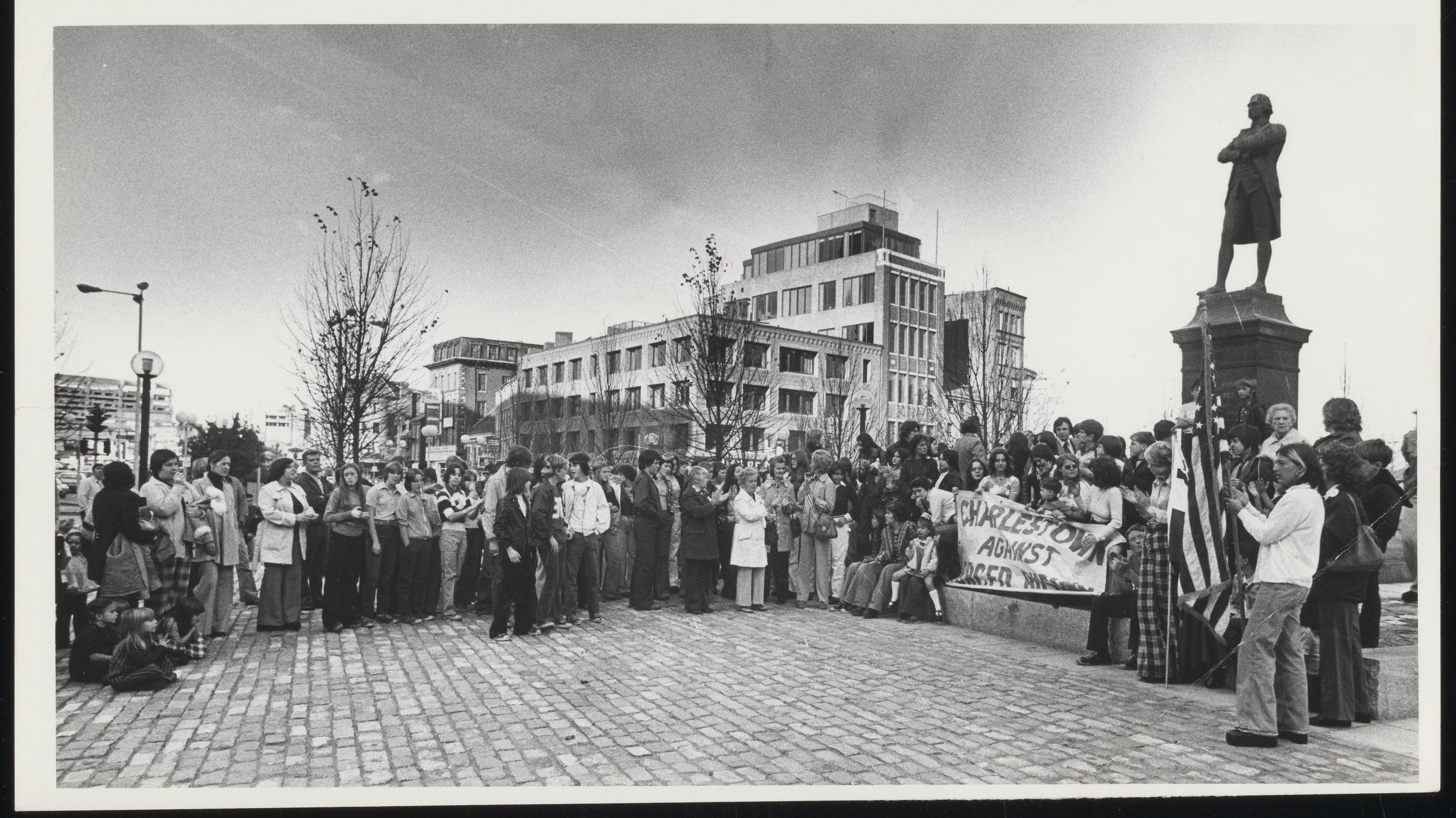 Black and white photo of a crowd surround the Sam Adams Statue 