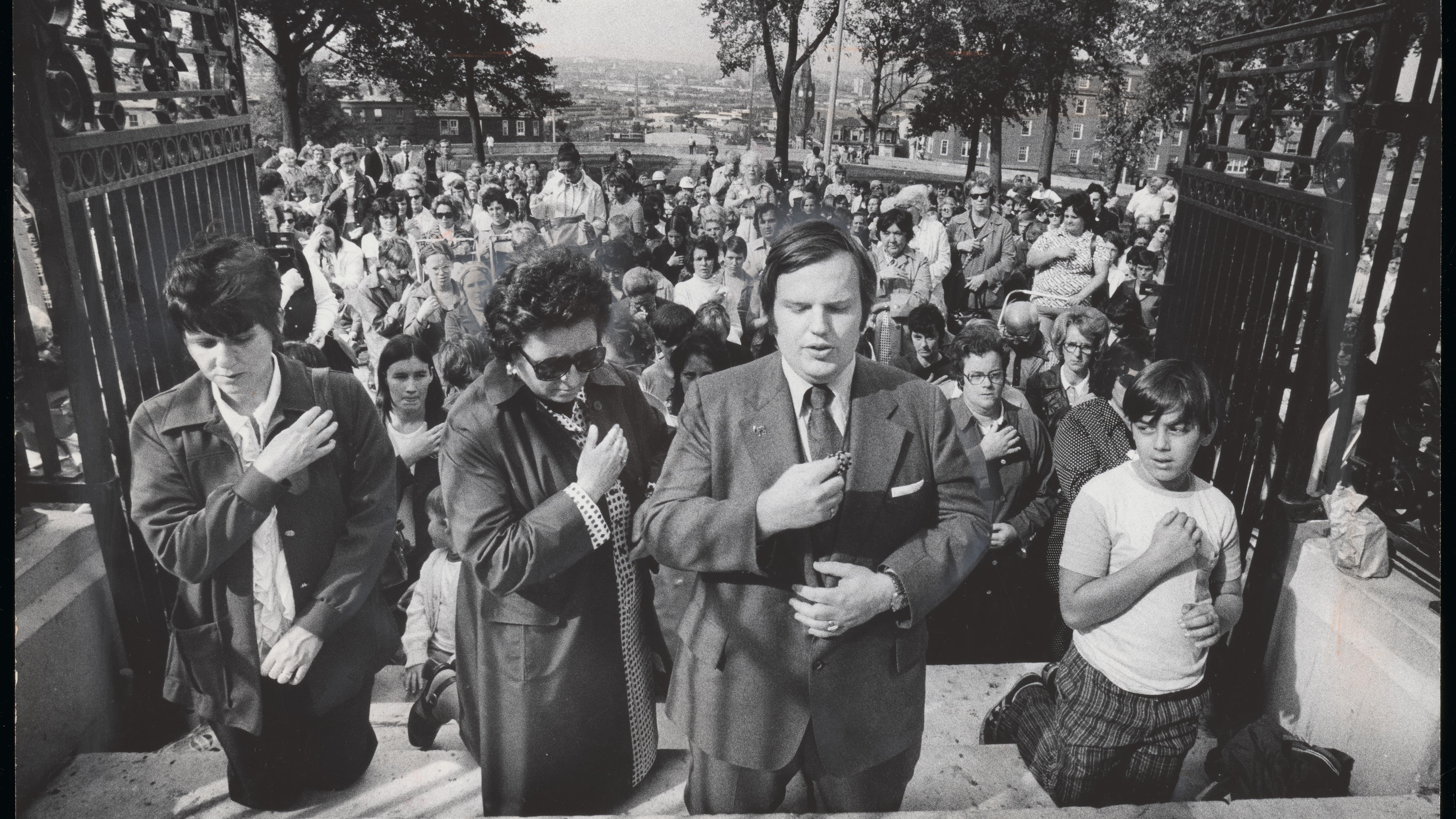 Black and white image of protestors kneeling on the steps of Dorchester Heights