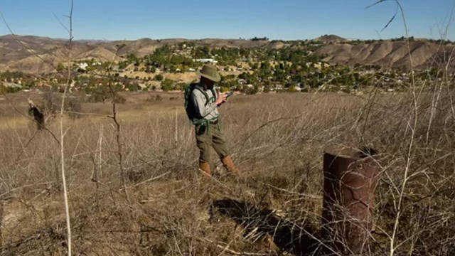 A worker standing next to a tube-shaped well using a GPS device.