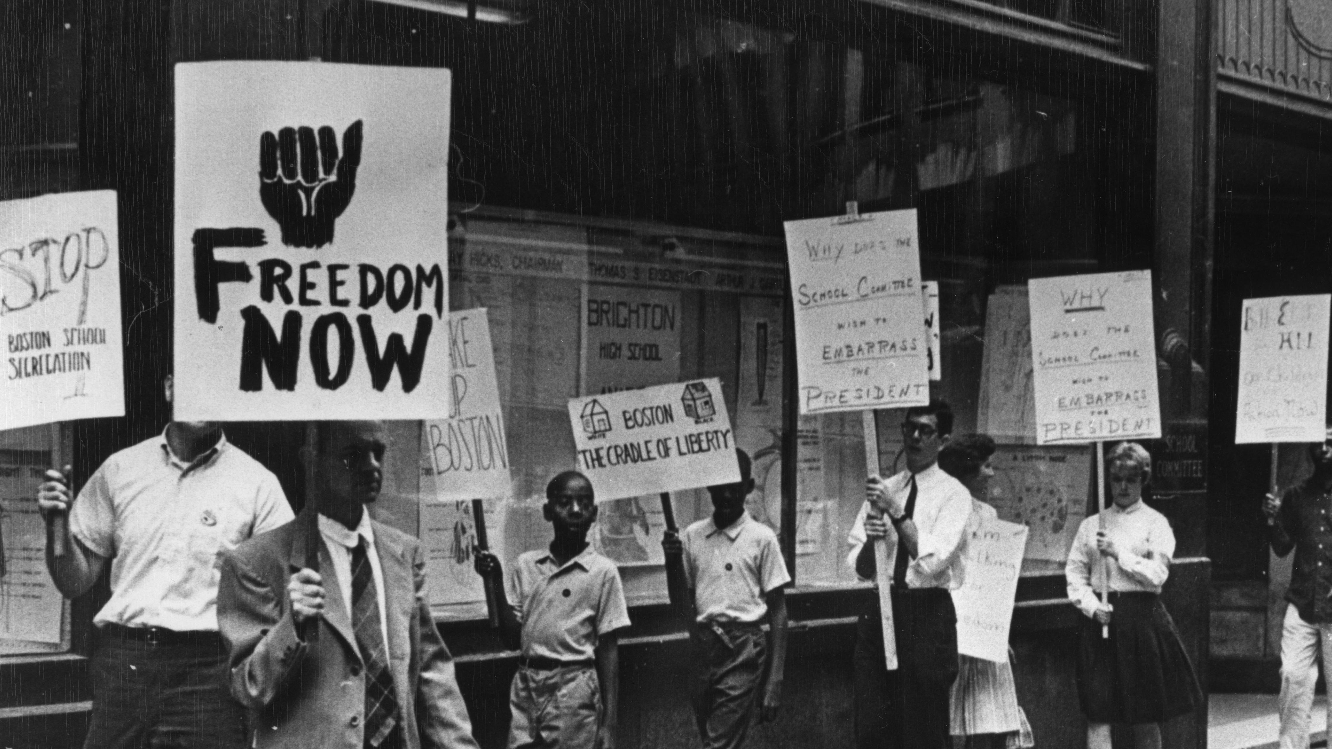Black and white photograph of protesters with different handwritten picket signs