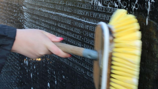A volunteer uses a cleaning brush to scrub the wall of names at the Vietnam Veteran&rsquo;s Memorial