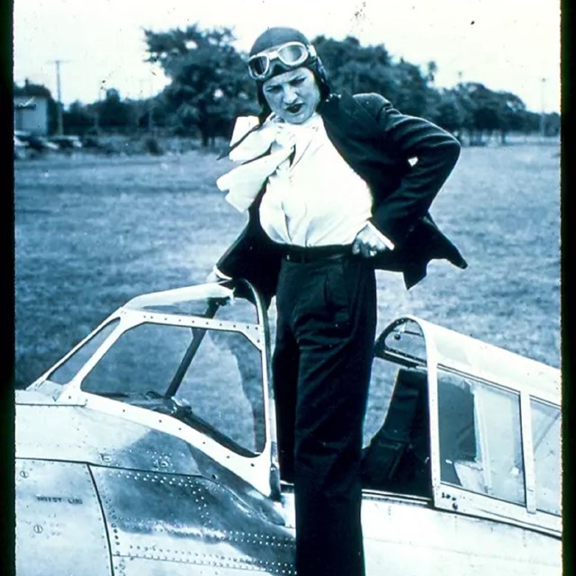 White woman in pilot's outfit adjusting clothes standing in plane cockpit