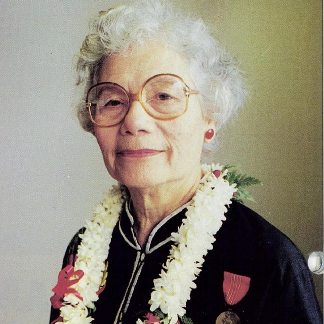 Portrait image of older Asian American woman wearing glasses wearing a lei