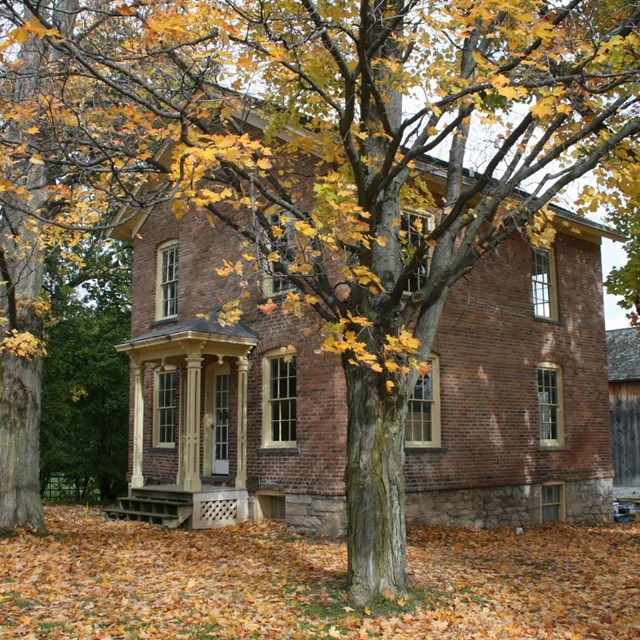 The front and side of a brick two-story house with small white columns in front and fall leaves