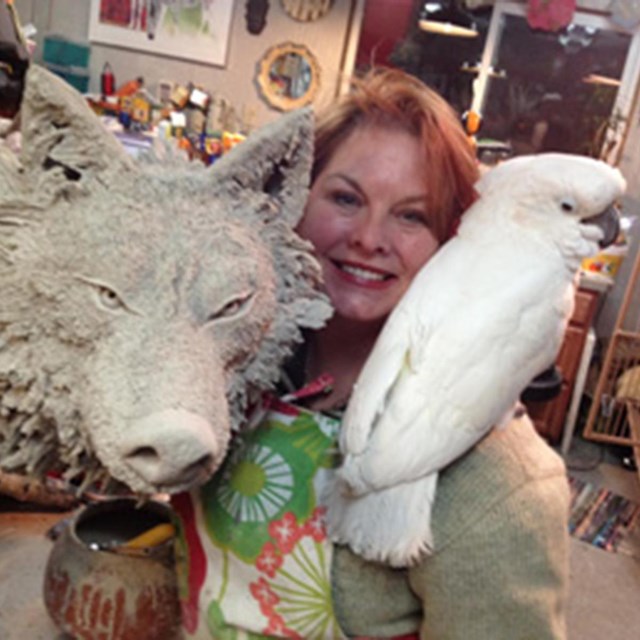 Gina in her studio with wolf sculpture and her cockatiel