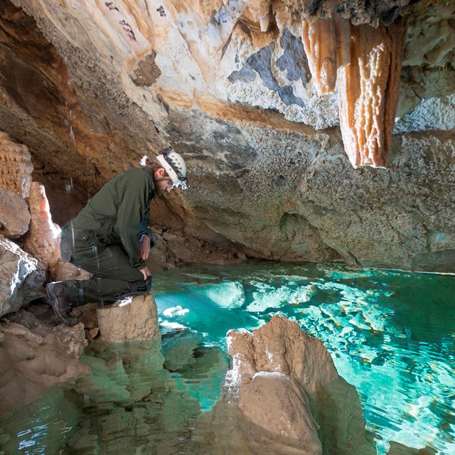 A caver looks into a natural pool in a cave