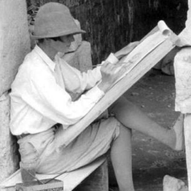 Portrait of Ann Morris seated on a box, painting at an archaeological site