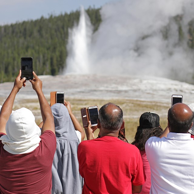 People taking a picture of an erupting geyser 