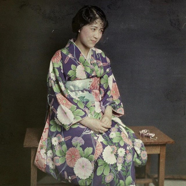 A woman with dark hair and wearing a floral patterned robe sits on a bench