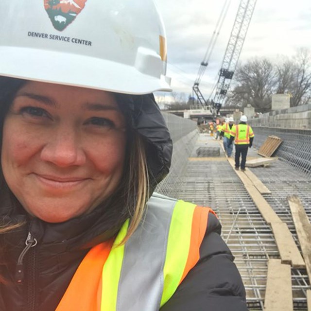Pamela looks into the camera. She is wearing a safety vest and hardhat