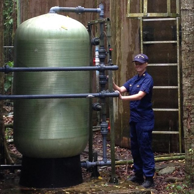 Kelly standing beside a large green water tank that dwarfs her in size.