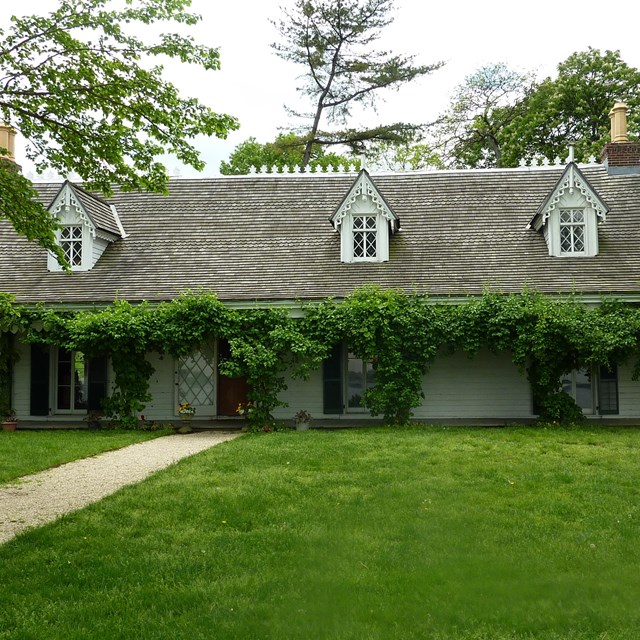 Facade of Alice Austen House: white siding, grey roof, greenery along roofline