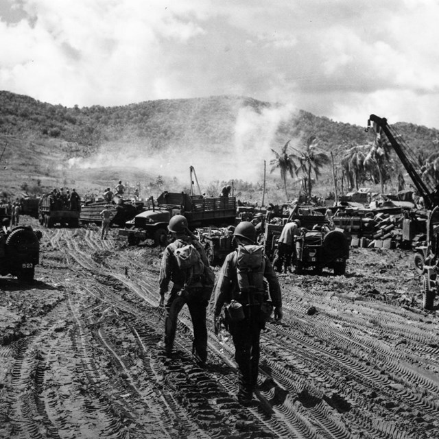 Soldiers in helmets and gear navigate a muddy area with military vehicles and equipment.