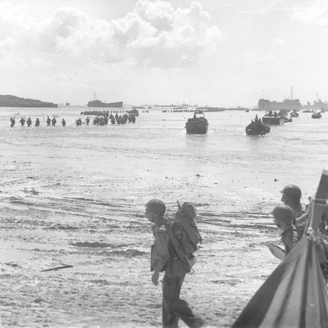 Soldiers wade through shallow waters toward the beach.