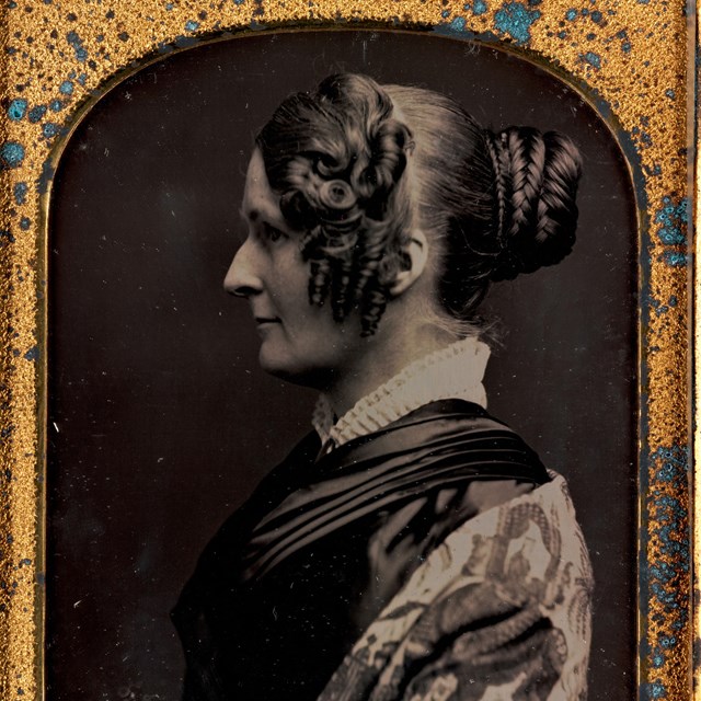 side profile of a woman wearing a dark dress with white collar and printed shawl.