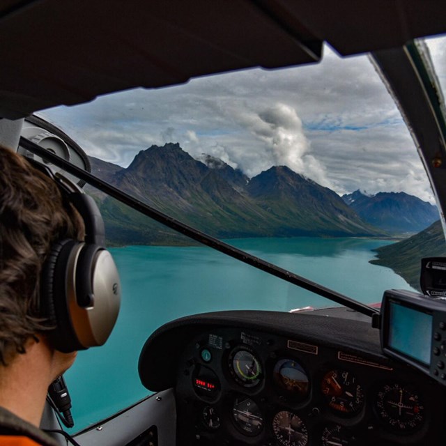 An NPS pilot looks out the cockpit window towards a turquoise lake