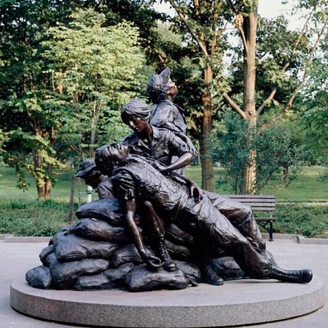 Statue of four human figures against background of trees and grass