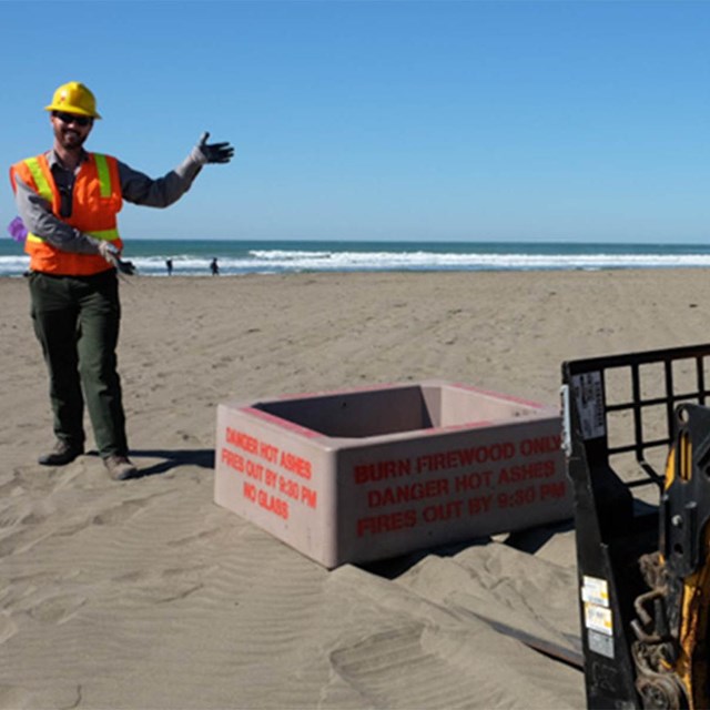 Person wearing safety gear guiding the installation of a fire pit at Ocean Beach