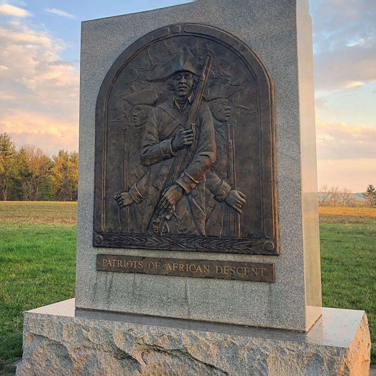 Stone monument with a metal engraving of a Black solider wearing a tricorn hat in a field