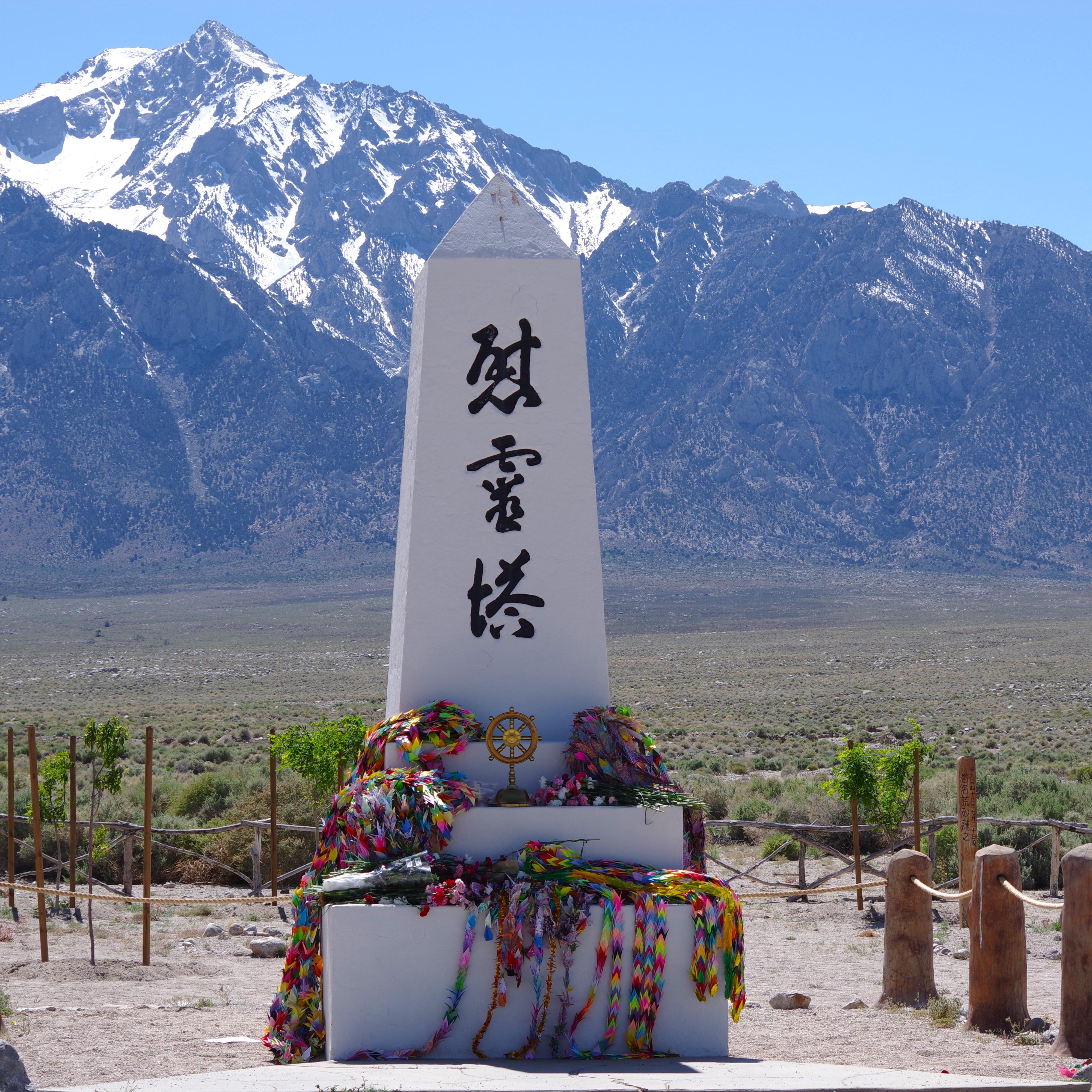 A white obelisk with kanji writing in front of a snowy mountain.