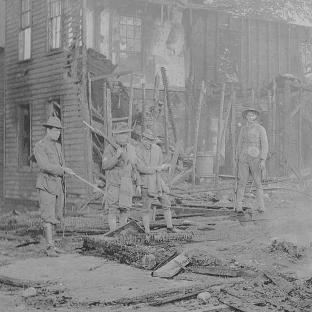 Historic photo of state militia members standing in the remains of a burned building.