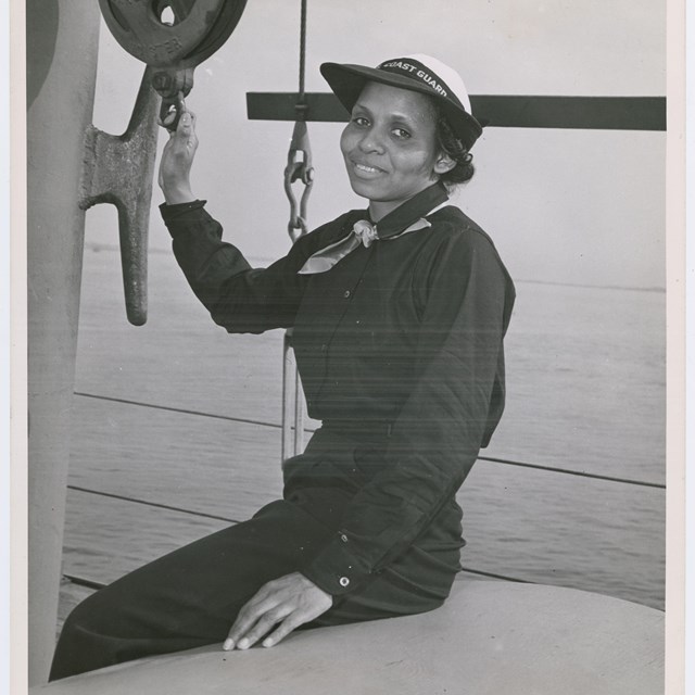 An African American woman in military uniform sits on the deck of a ship